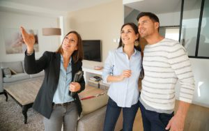 Real estate agent guiding a couple through a modern living room during a home tour, she points to features.