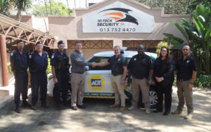 Group of security guards posing in front of a Hi-Tech Security sign and an ADT patrol car; two men shake hands in the center.