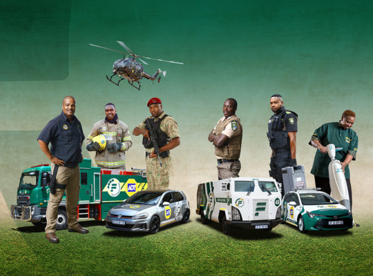 Diverse emergency responders—firefighter, police, and paramedics—standing with emergency vehicles and a helicopter in a staged team photo on grass.