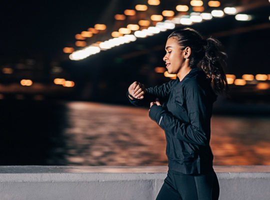 Young middle east woman jogging at night looking in fitness tracker on her wrist